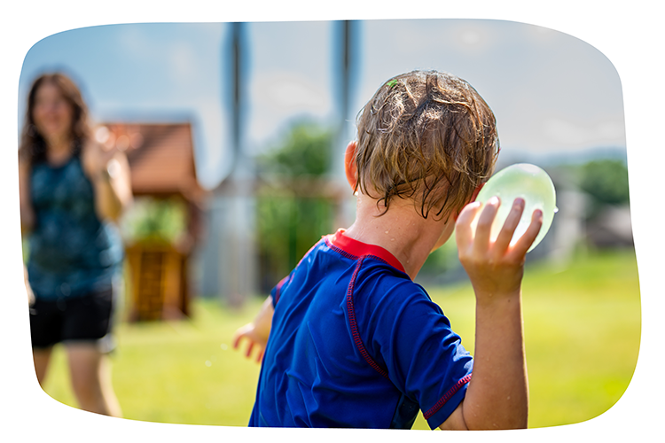 Ein Kind spielt im Garten. Es hält einen Wasserball in der Hand.