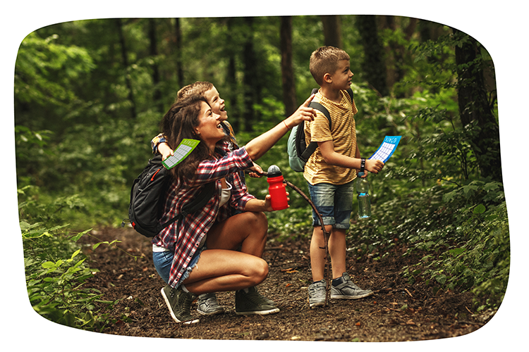 Ein Erwachsener und zwei Kinder stehen im Wald. Sie haben Rucksäcke und halten eine Karte in der Hand.