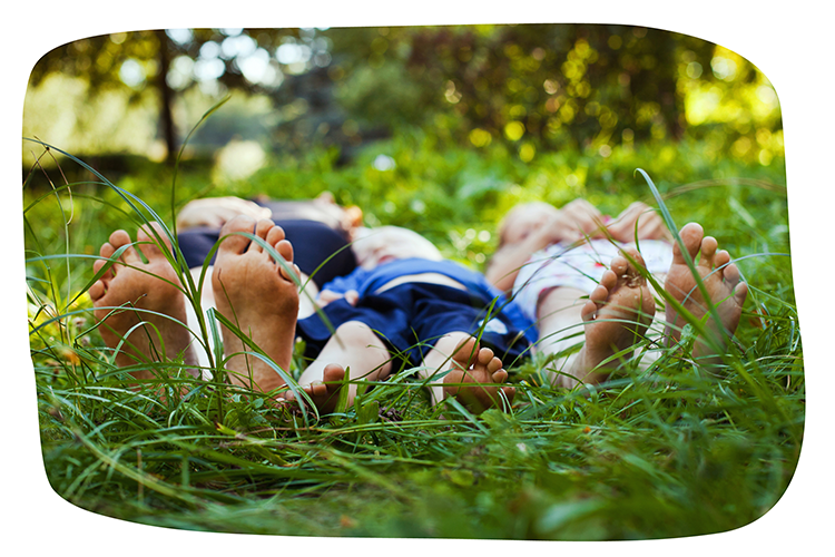Drei Personen liegen barfuß auf einer grünen Wiese. Die Sonne scheint.